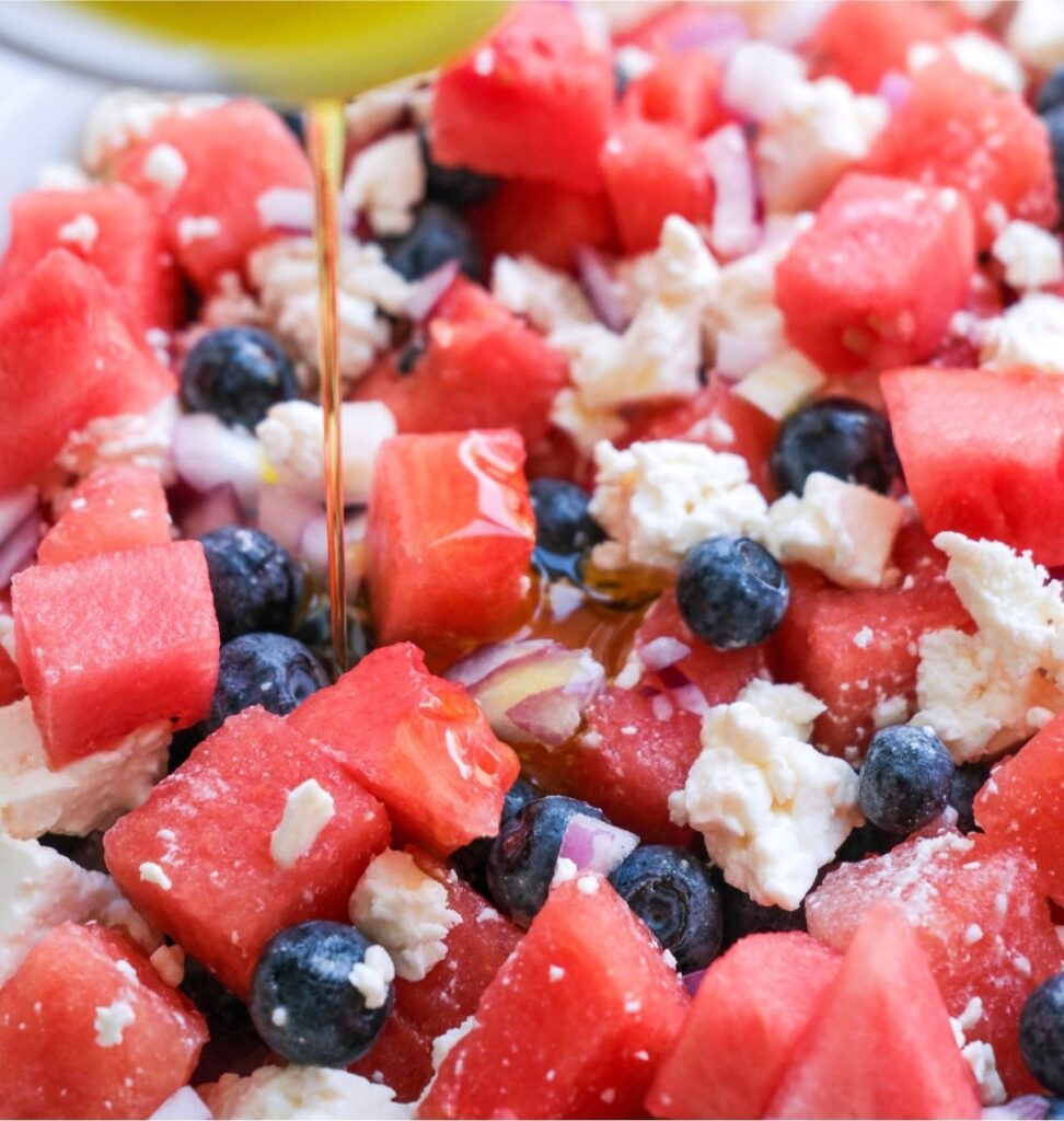 Close-up of a refreshing salad featuring juicy watermelon cubes, sweet blueberries, tangy crumbled feta, and a drizzle of olive oil.