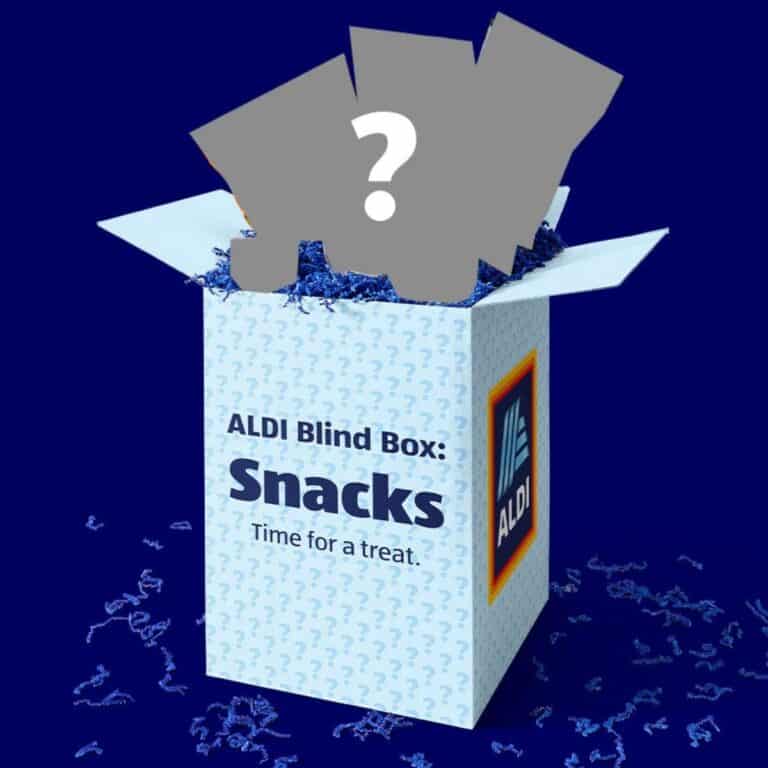 A box labeled "ALDI Blind Box: Snacks" with blue shredded paper inside and three mystery snack items silhouetted above the open box, featured as part of exciting ALDI promotions.