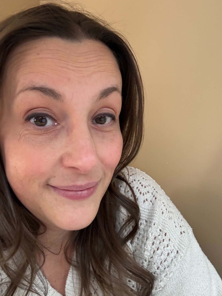 A woman with long brown hair and a white knit sweater smiles slightly while looking at the camera against a beige background, as if pondering what I learned from a simple question.