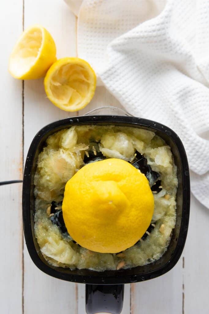 Lemon juicer in use with a halved lemon, two squeezed halves, and a white towel on wood.